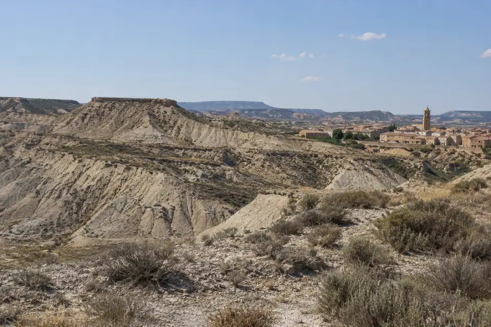 Een kale steppe van bleke klei met tafelbergen, en okerkleurige huizen rond een bakstenen klokkentoren.