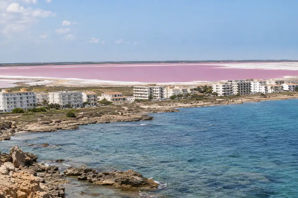 Vlakke stad met witte appartementenblokken langs een rotsige kust, met een roze zoutmeer erachter.