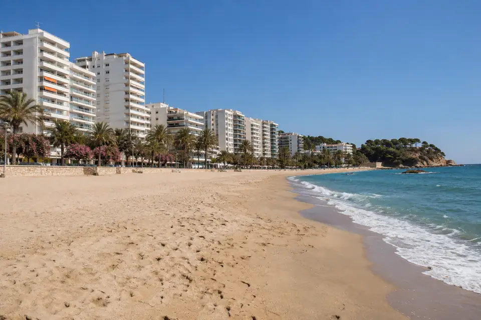 Lang zandstrand met een rechte rij hoge witte flats met balkons en een palmenboulevard.