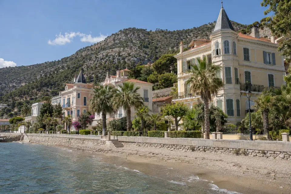 Grote negentiende-eeuwse villa's met hoektorens en palmtuinen staan achter een smalle strook zand.
