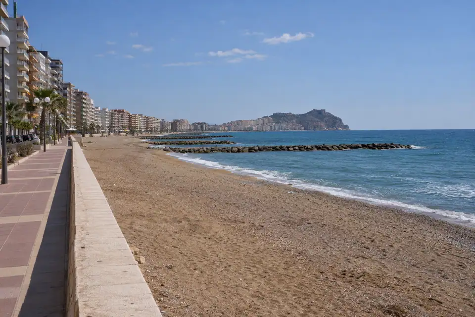 Kilometerslang recht strand met een onafgebroken rij gelijkvormige flats en lage stenen golfbrekers.