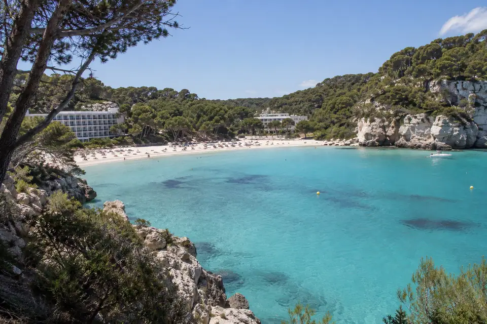 Hoefijzervormige baai met wit zand tussen hoge kliffen met pijnbossen, en zeer licht turquoise water.