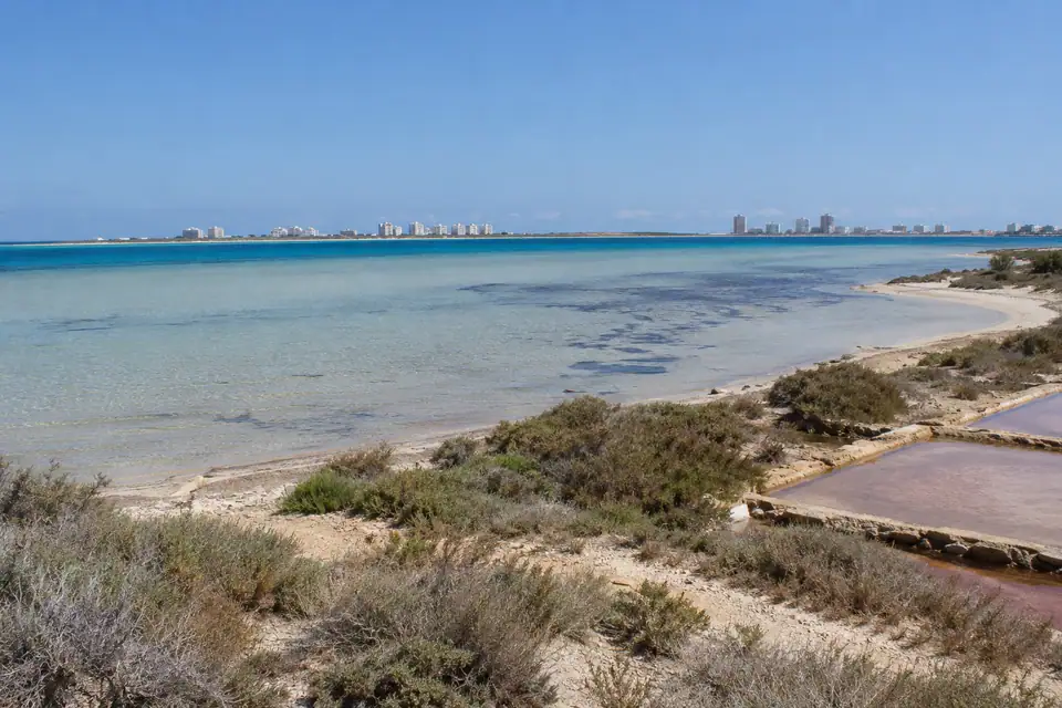 Zeer ondiepe blauwgroene lagune met vlak zandstrand, aan de overkant een lange zandbank met witte flats.