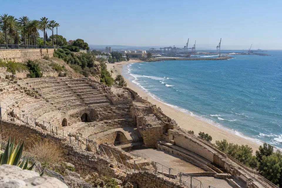 Verweerde stenen zitrijen van een ovale Romeinse arena in een helling boven een zandstrand.