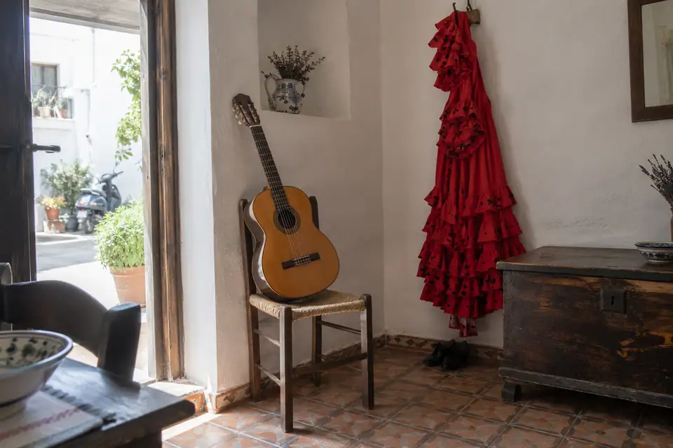 Een klassieke gitaar op een rieten stoel en een rode flamencojurk aan de witte wand.