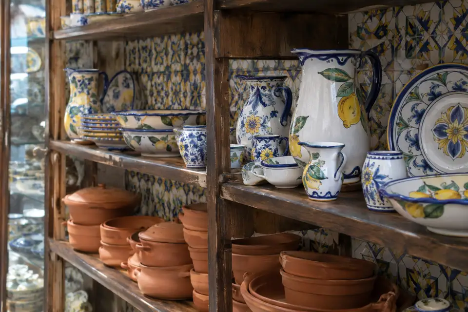 Houten schappen vol handbeschilderd aardewerk in wit met kobaltblauw, geel en groen, met terracottaschalen eronder.