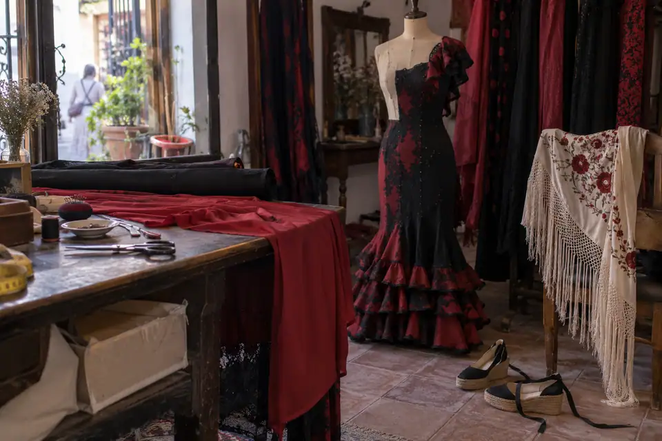 Werktafel met rollen zwarte en rode stof, paspop met half opgespelde jurk en geborduurde zijden omslagdoek.