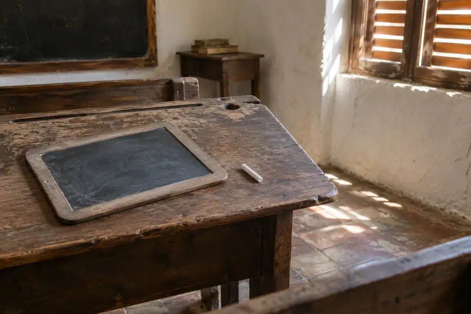 Versleten houten schoolbank met een lege zwarte lei en een stukje krijt erop.