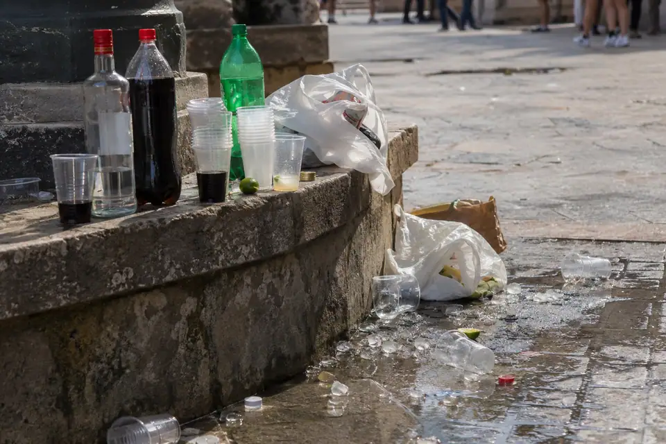 Plastic drankflessen en stapels bekers op een laag muurtje, met zwerfafval op de stenen.