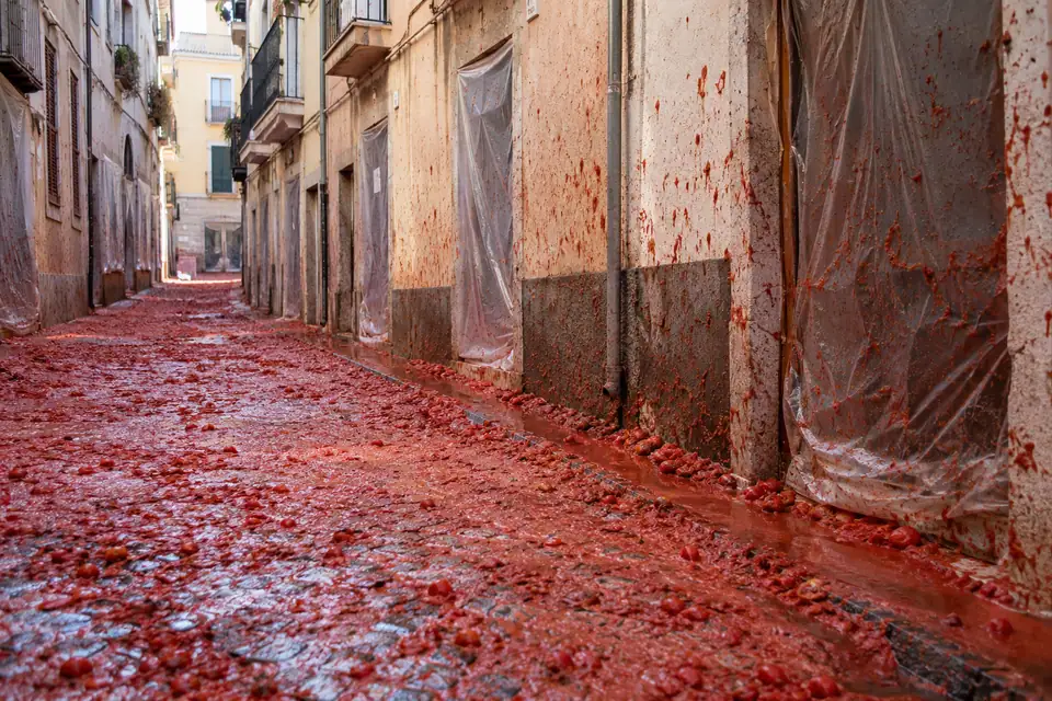 Smalle straat met kasseien onder een laag geplette tomaten, rode spatten op de onderste muren.