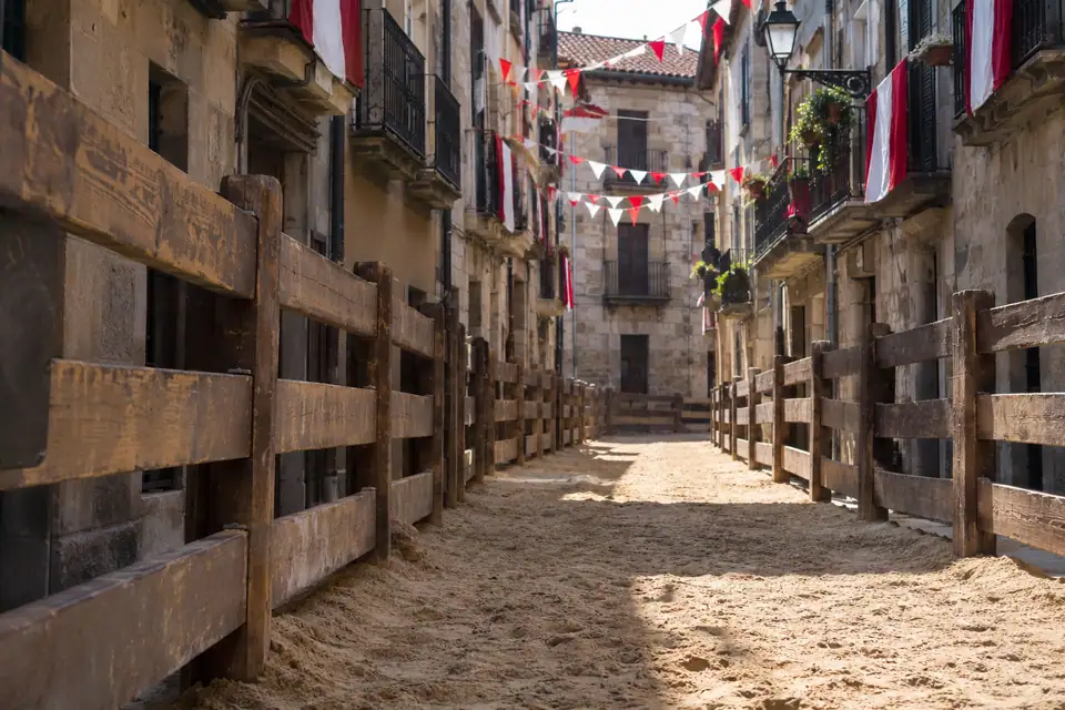 Zware houten schotten langs een smalle straat met zand, rood-witte vlaggetjes aan de balkons.