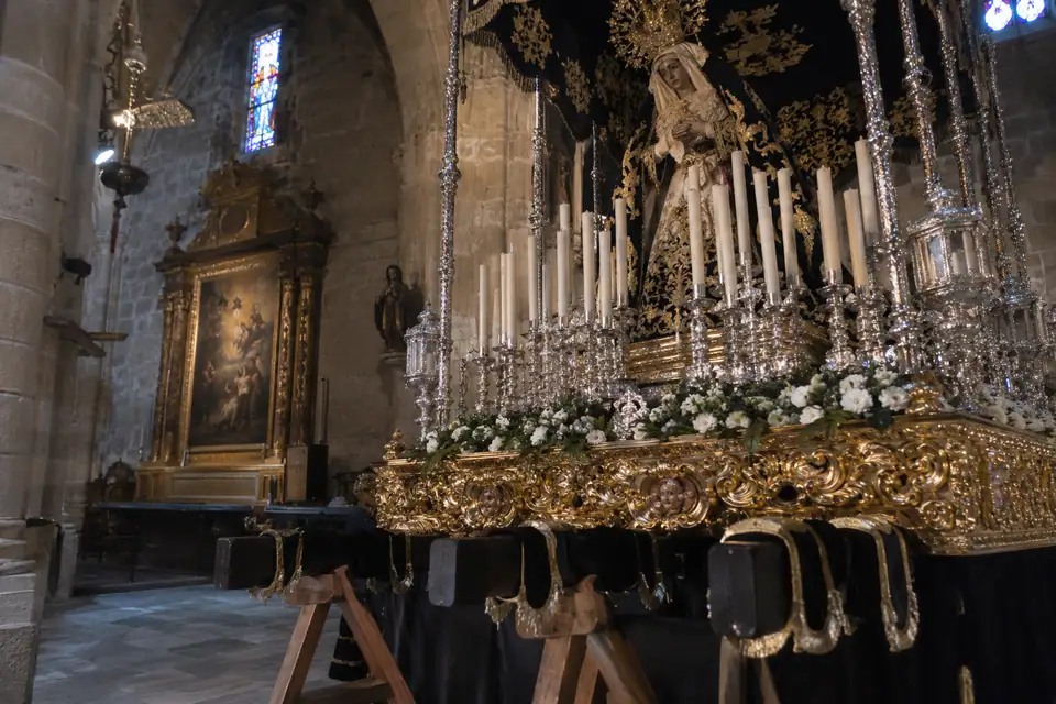 Vergulde processiewagen met beeld onder fluwelen baldakijn en rijen hoge witte kaarsen in een kerk.