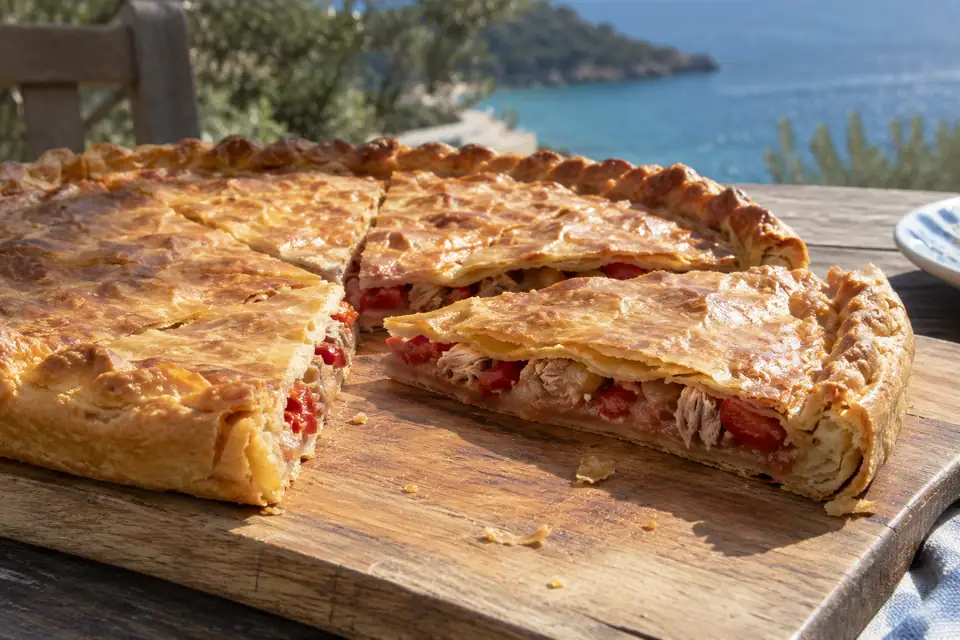 Grote ronde platte taart met goudbruin deegdeksel, in punten gesneden met zichtbare tonijnvulling.