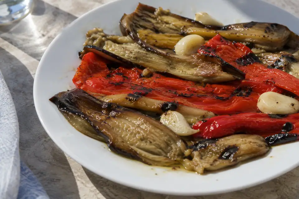 Repen geroosterde aubergine en rode paprika met zwartgeblakerde randen, glanzend van olijfolie op een bord.