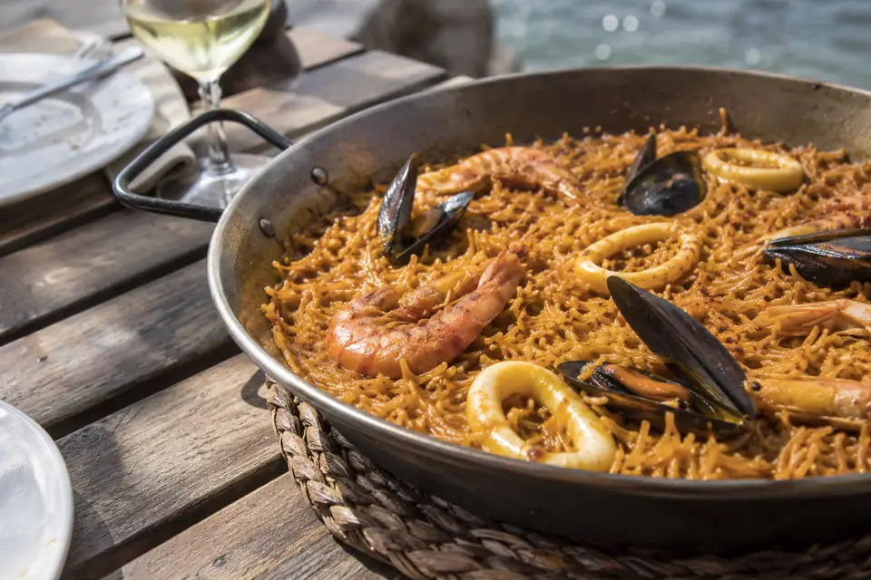 Wijde platte pan met korte dunne noedels die rechtop staan, met garnalen en mosselen ertussen.