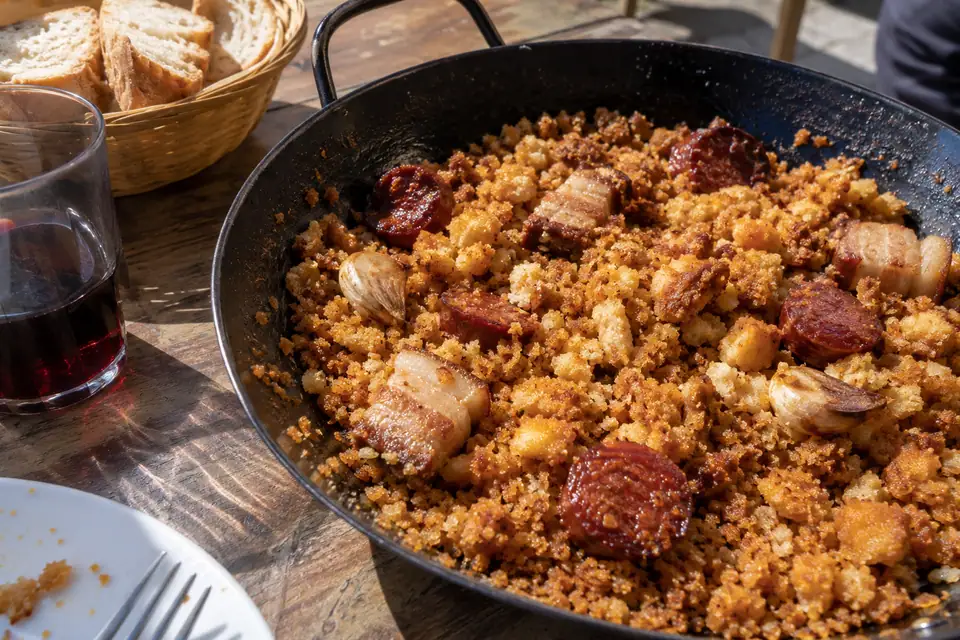Zwarte koekenpan met grof gebakken broodkruim, schijven donkerrode chorizo en hele knoflooktenen.