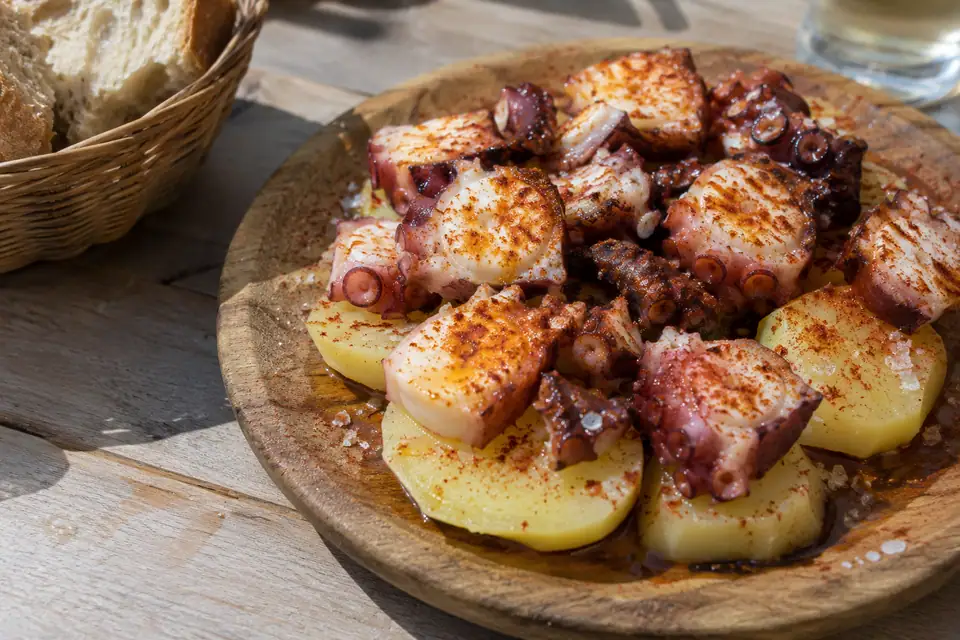 Dikke schijven octopus met zichtbare zuignappen op gekookte aardappelschijfjes, bestrooid met grof paprikapoeder en zout.