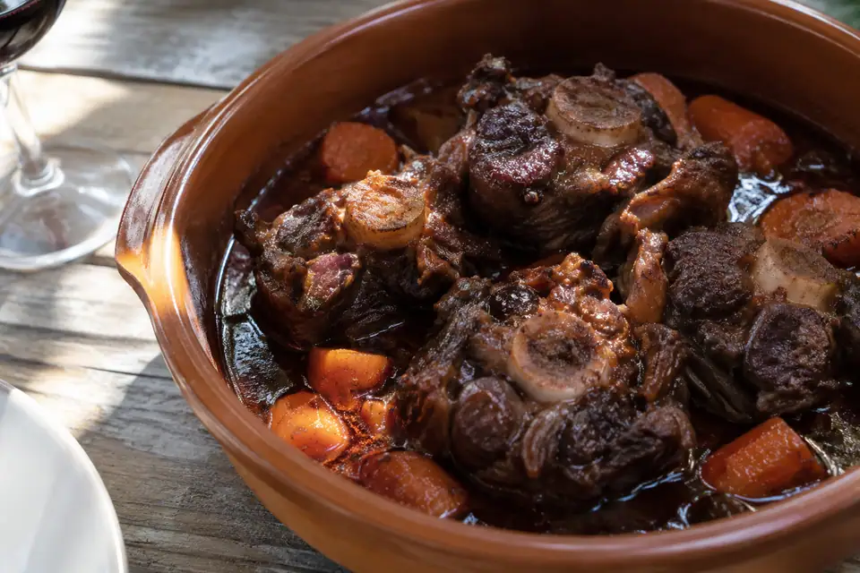 Dikke stukken ossenstaart met het bot in het midden in een donkere glanzende saus.