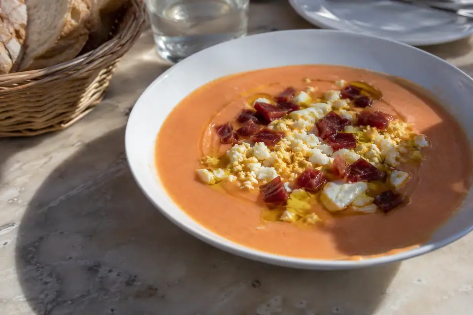 Ondiepe schaal met dikke lichtroze tomatencrème, bestrooid met verkruimeld ei en blokjes gedroogde ham.