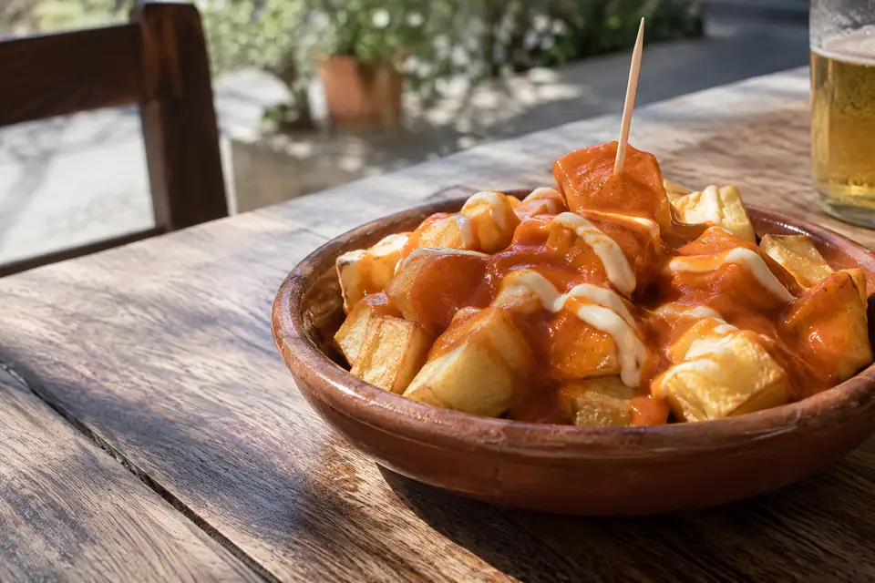 Grove blokken gebakken aardappel in een aardewerken schaaltje met oranje saus en witte knoflookmayonaise.