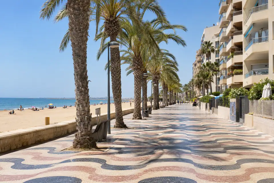 Stadsstrand met een boulevard van tegels met golvend patroon, kale grijze kalkrots erachter.